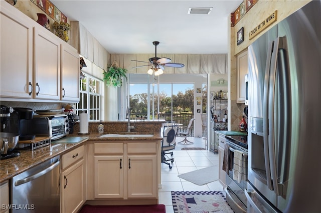 kitchen with stainless steel appliances, dark stone counters, sink, light tile patterned floors, and ceiling fan