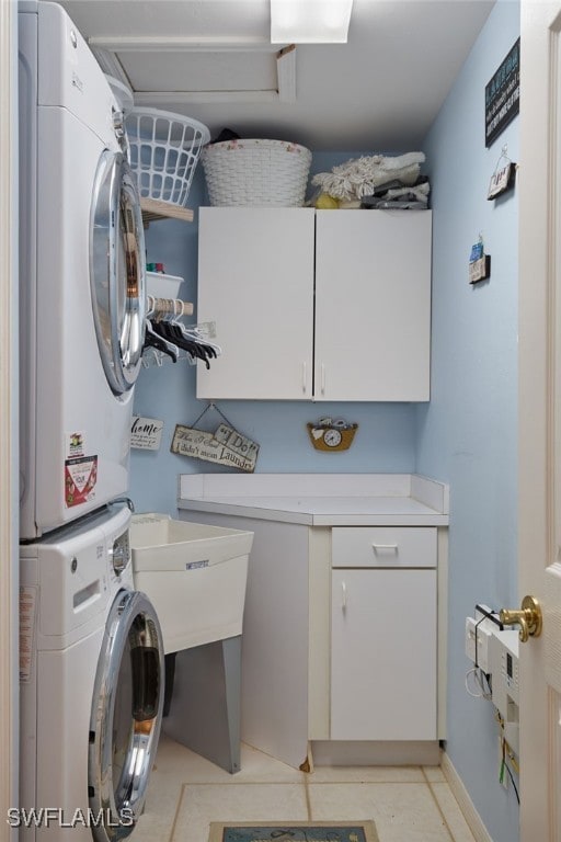 washroom featuring stacked washing maching and dryer, light tile patterned flooring, and cabinets