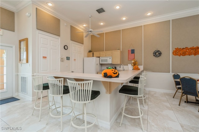 kitchen with a breakfast bar, ornamental molding, ceiling fan, and white appliances