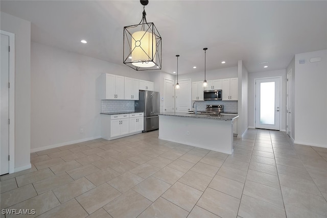 kitchen featuring tasteful backsplash, appliances with stainless steel finishes, hanging light fixtures, white cabinets, and a kitchen island with sink