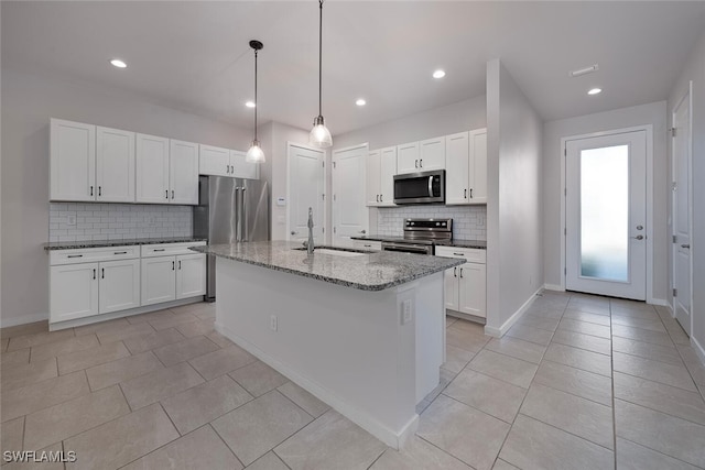 kitchen featuring a kitchen island with sink, stainless steel appliances, dark stone countertops, sink, and white cabinets