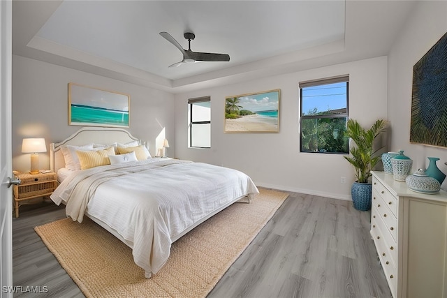 bedroom with ceiling fan, a tray ceiling, and light hardwood / wood-style flooring