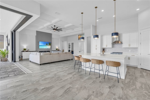 kitchen with wall chimney range hood, hanging light fixtures, a large island, coffered ceiling, and white cabinets