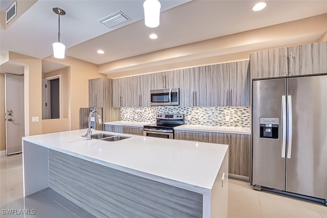 kitchen with a kitchen island with sink, hanging light fixtures, backsplash, sink, and appliances with stainless steel finishes