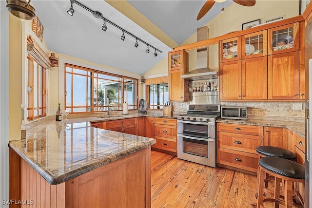 kitchen with wall chimney exhaust hood, light stone counters, vaulted ceiling, double oven range, and kitchen peninsula