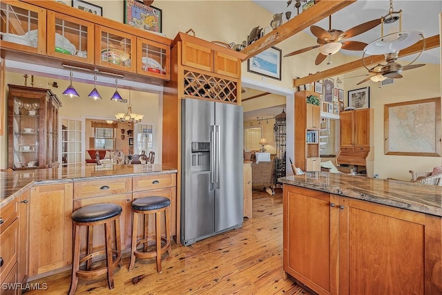 kitchen featuring light hardwood / wood-style flooring, stainless steel fridge, a high ceiling, decorative light fixtures, and dark stone counters