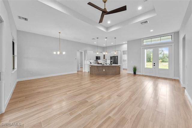 unfurnished living room featuring french doors, light hardwood / wood-style flooring, sink, a raised ceiling, and ceiling fan with notable chandelier