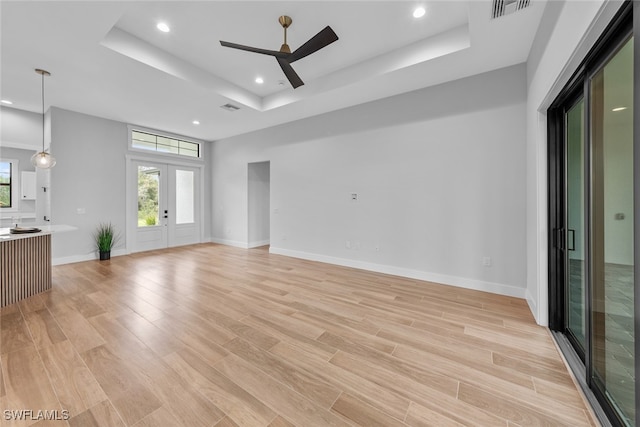 unfurnished living room with french doors, a tray ceiling, light wood-type flooring, and ceiling fan