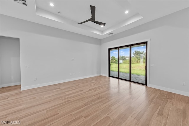 empty room featuring a tray ceiling and light wood-type flooring