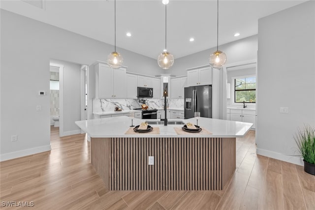 kitchen with appliances with stainless steel finishes, hanging light fixtures, white cabinets, and an island with sink