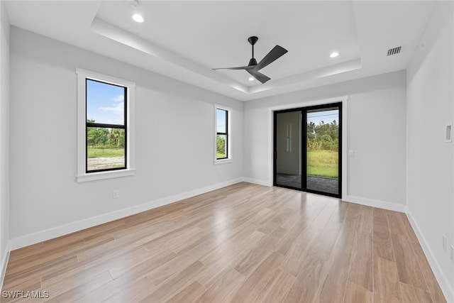 spare room with ceiling fan, a raised ceiling, a wealth of natural light, and light wood-type flooring