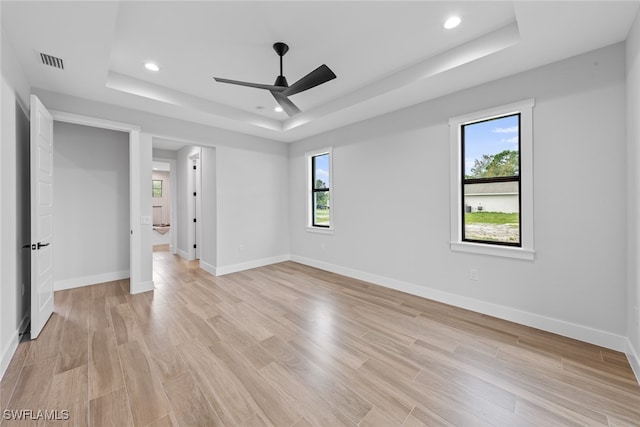 unfurnished bedroom with light hardwood / wood-style floors, ceiling fan, and a raised ceiling