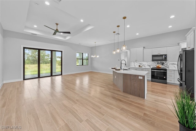 kitchen with white cabinets, a healthy amount of sunlight, black appliances, and an island with sink