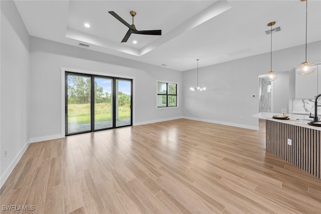 unfurnished living room with a tray ceiling, ceiling fan with notable chandelier, and light hardwood / wood-style floors