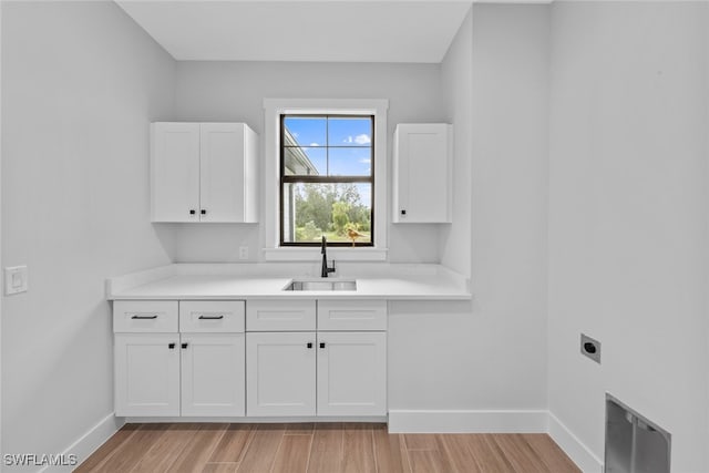 clothes washing area with hookup for an electric dryer, sink, light hardwood / wood-style floors, and cabinets