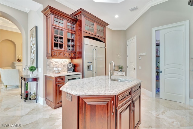 kitchen with a center island with sink, built in refrigerator, decorative backsplash, crown molding, and sink