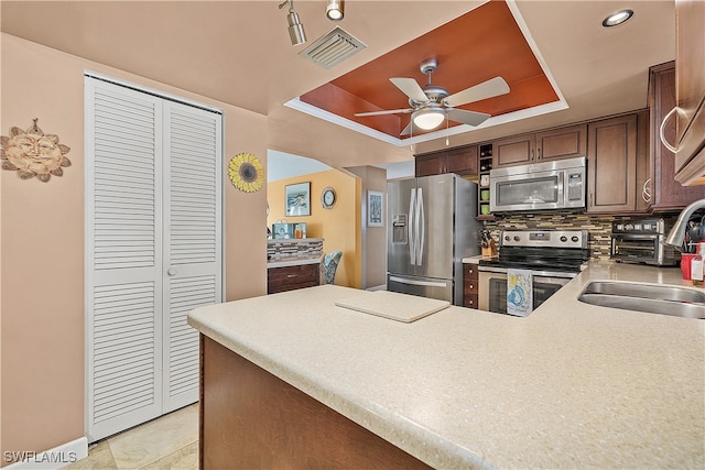 kitchen with sink, appliances with stainless steel finishes, kitchen peninsula, and a tray ceiling