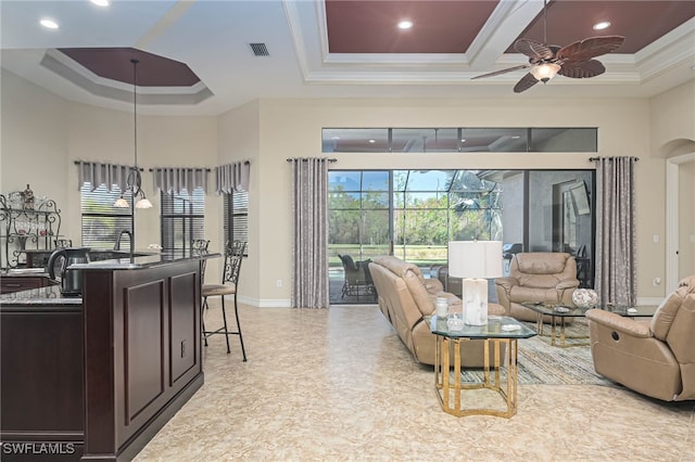 living room with a towering ceiling, ceiling fan, ornamental molding, and a tray ceiling