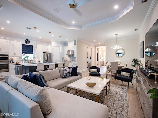 living room with light hardwood / wood-style flooring, ornamental molding, a tray ceiling, and ceiling fan with notable chandelier