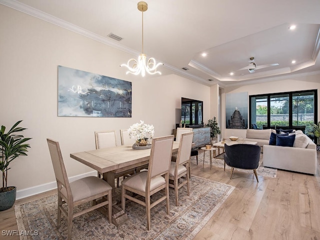 dining space featuring crown molding, ceiling fan with notable chandelier, light hardwood / wood-style floors, and a raised ceiling