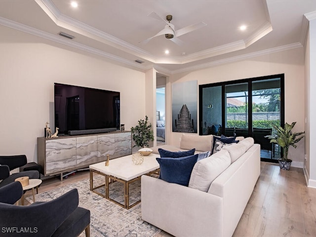 living room featuring crown molding, ceiling fan, light wood-type flooring, and a raised ceiling