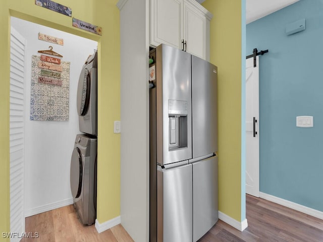 laundry area featuring stacked washing maching and dryer, a barn door, and light hardwood / wood-style floors