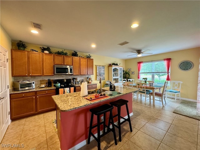 kitchen with a center island with sink, a kitchen bar, ceiling fan, appliances with stainless steel finishes, and tasteful backsplash