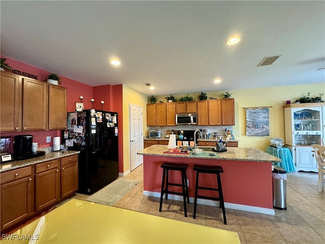 kitchen with light stone countertops, black appliances, backsplash, a breakfast bar area, and a kitchen island with sink