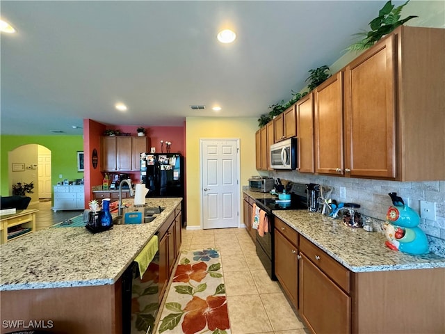 kitchen featuring light tile patterned floors, backsplash, an island with sink, black appliances, and sink