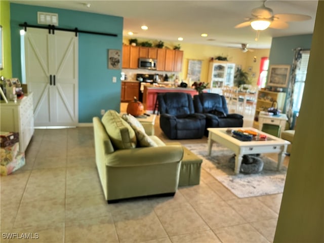 living room with a barn door, ceiling fan, and light tile patterned floors