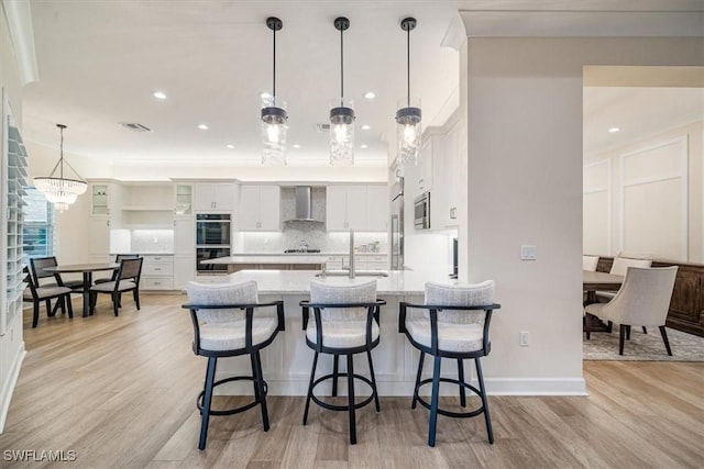 kitchen with a sink, a kitchen bar, wall chimney range hood, and double wall oven