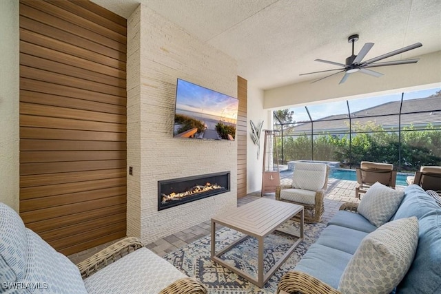 living area featuring a glass covered fireplace, a ceiling fan, a sunroom, and a textured ceiling