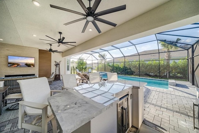 view of patio featuring an outdoor pool, ceiling fan, glass enclosure, and an outdoor kitchen