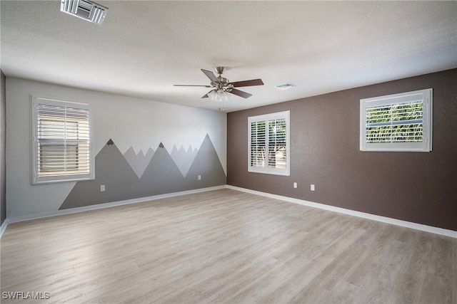 spare room featuring a textured ceiling, light wood-type flooring, a healthy amount of sunlight, and ceiling fan