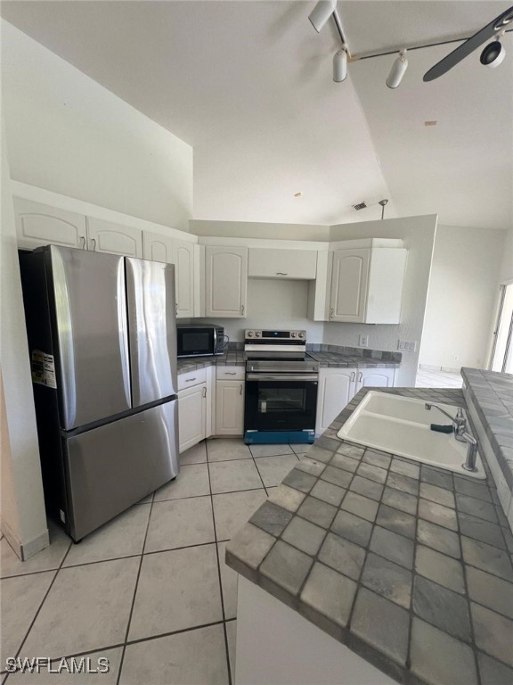 kitchen featuring tile counters, kitchen peninsula, stainless steel appliances, vaulted ceiling, and white cabinets