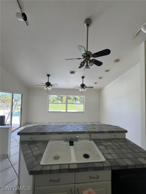 kitchen featuring tile counters, dishwashing machine, sink, light tile patterned flooring, and vaulted ceiling