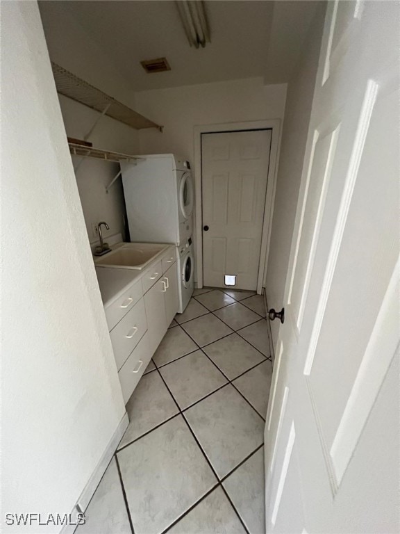 laundry room featuring sink, stacked washer / drying machine, cabinets, and light tile patterned floors