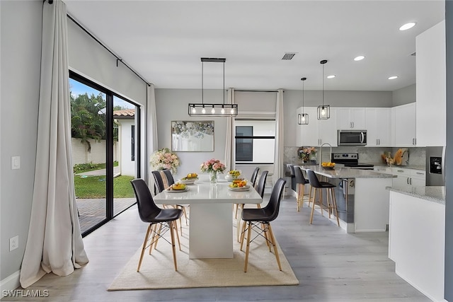 kitchen with white cabinets, a kitchen island with sink, a kitchen bar, light hardwood / wood-style flooring, and stainless steel appliances