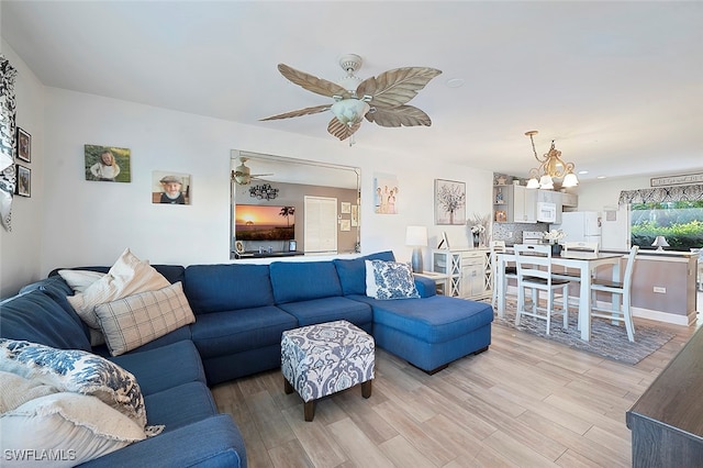 living room with ceiling fan with notable chandelier and light hardwood / wood-style flooring