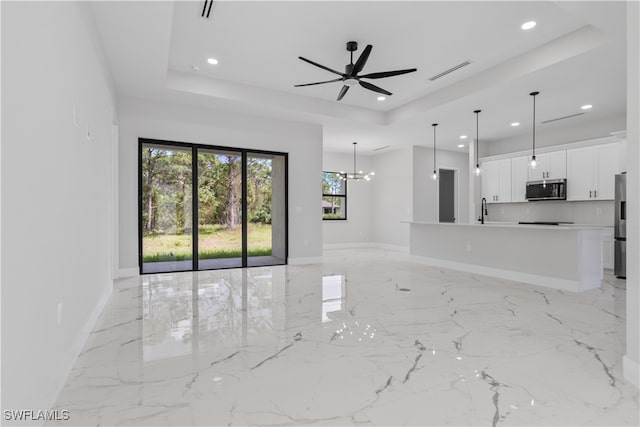 unfurnished living room with a raised ceiling, sink, and ceiling fan with notable chandelier