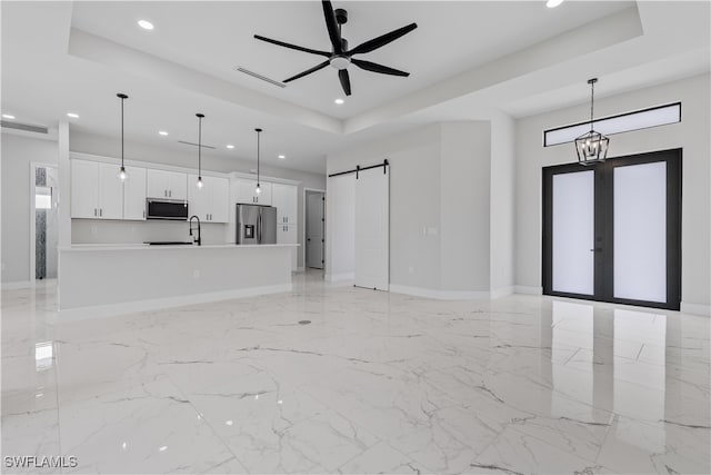 unfurnished living room featuring ceiling fan with notable chandelier, a raised ceiling, sink, and a barn door