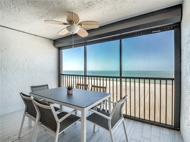 sunroom featuring ceiling fan, a view of the beach, and a water view