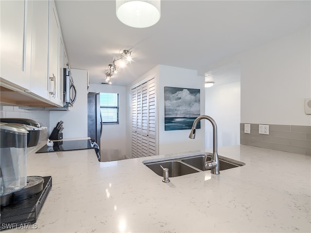 kitchen featuring stainless steel appliances, light stone countertops, white cabinetry, and sink