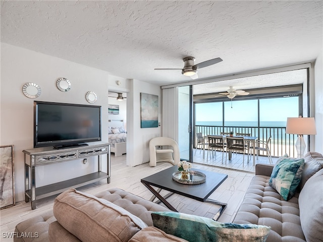 living room featuring light wood-type flooring, a textured ceiling, a water view, and floor to ceiling windows