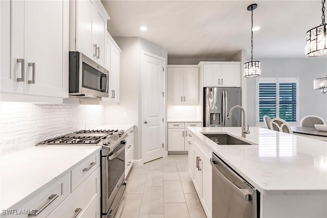 kitchen with a kitchen island with sink, stainless steel appliances, sink, pendant lighting, and white cabinetry