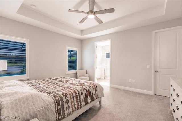 bedroom featuring ensuite bathroom, a tray ceiling, and ceiling fan