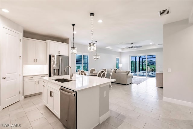 kitchen with appliances with stainless steel finishes, white cabinets, a center island with sink, and pendant lighting