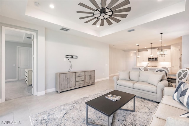 tiled living room featuring a tray ceiling and ceiling fan with notable chandelier