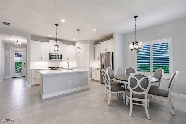 kitchen with appliances with stainless steel finishes, pendant lighting, white cabinets, and an island with sink