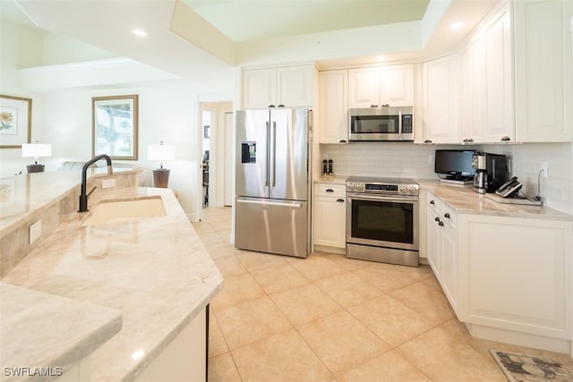 kitchen featuring white cabinets, appliances with stainless steel finishes, light stone counters, and sink